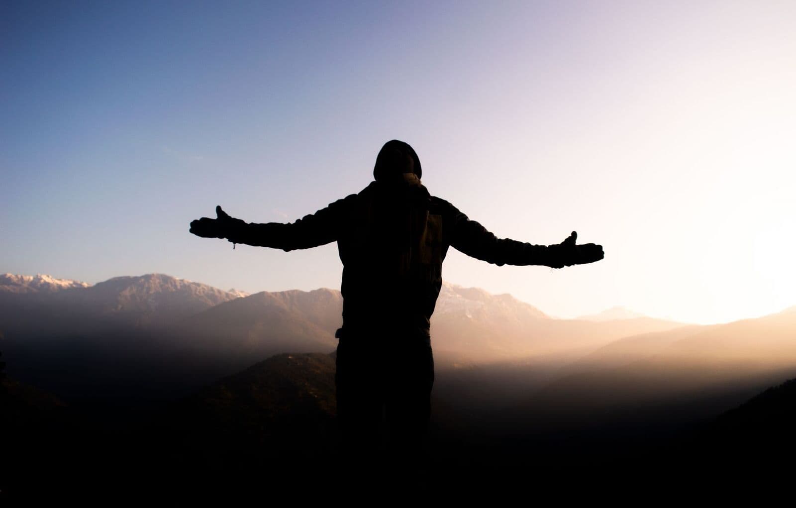 Person with arms open in a field at sunrise